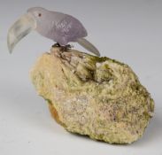 A quartz toucan with clear bill and pink body, cabochon red stone eyes and silver claws gripping a