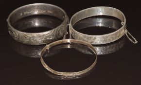 Three silver bangles, two with floral decoration