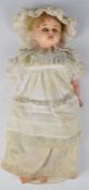 A wax over composition doll of a young girl with blonde hair, blue weighted eyes, white dress and