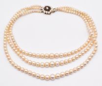 A triple strand cultured pearl necklace, the 9ct gold clasp set with garnets and pearls, 63g, 35cm