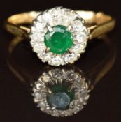 An 18ct gold ring set with a round cut emerald surrounded by diamonds in a platinum setting, 3.6g,