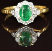 An 18ct gold ring set with an oval cut emerald of approximately 0.6ct surrounded by diamonds, 3g,