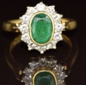 An 18ct gold ring set with an oval cut emerald of approximately 1.5ct surrounded by diamonds, 8.