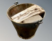 A brass swing handled bucket containing a small quantity of firewood.