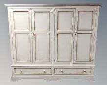 A contemporary cream four door wardrobe fitted with two drawers beneath.