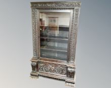 A Victorian heavily carved oak glazed door bookcase fitted with a drawer beneath.