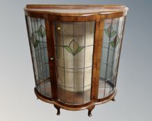 A walnut bow fronted display cabinet with leaded glass doors.