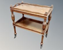 An Edwardian carved oak two tier drinks trolley on castors.