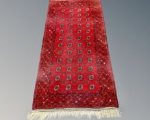An Afghan fringed rug on red ground,