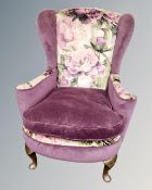 An Art Deco style wingback armchair upholstered in a purple floral fabric.