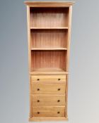 A set of narrow open bookshelves, fitted with four drawers beneath,