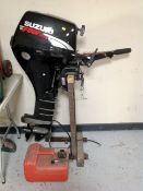 A Suzuki four stroke outboard motor on stand with petrol can