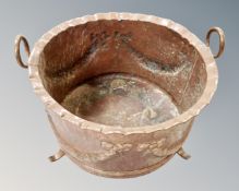 A 19th century copper embossed twin handled cooking pot on raised feet,