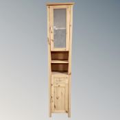 A narrow pine glazed door cabinet fitted with shelves and cupboard