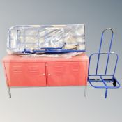 A metal double door workshop cabinet on raised legs together with a newspaper trolley and further