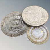 A brass embossed wall plaque depicting a galleon together with two further eastern brass table tops