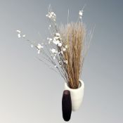 A ceramic pot together with artificial flowers and sticks and a glass vase.
