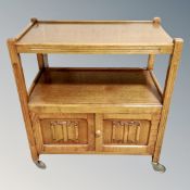 An oak linen fold serving trolley with cupboards below