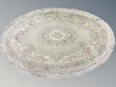 A Chinese oval fringed rug on pale green ground,