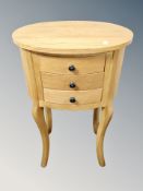 A contemporary oval pine three drawer bedside stand