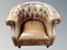 A contemporary armchair in deep buttoned chestnut brown leather,