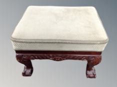 A carved footstool on claw and ball feet,