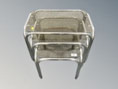 A contemporary nest of three chrome and glass tables