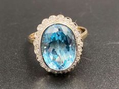 A Swiss, blue topaz and diamond set, 9ct yellow gold, “Illusion” halo ring.