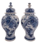 A pair of Dutch Delft blue and white baluster vases and covers each painted with buildings by a