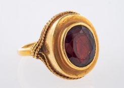 An 18ct yellow gold ring set with an oval-cut garnet in a collet and rope twist setting, size O 1/2,