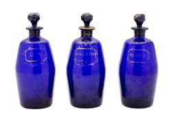 A group of three 'Bristol' blue glass barrel-shaped decanters and faceted stoppers with gilt labels