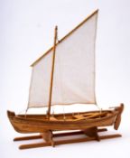 A scale model of a lugger boat 'Astrid' set sail over planked hull, raised on a wooden cradle,