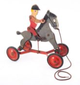 A mid 20th century tin and wooden huntsman riding a horse pull along toy
