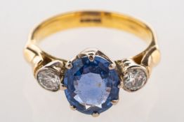 A three stone sapphire and diamond ring, claw set to the centre with an oval-cut sapphire,
