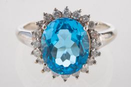 A 9ct white gold blue topaz and diamond cluster ring, claw set with an oval-cut blue topaz, approx.