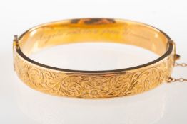 A 1920's 9ct gold bangle, with floral and foliate engraving to the front, hinged, safety chain,