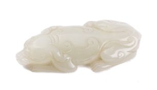 A Chinese jade carving of a crouching dog its head resting on its forelegs with tail curled beneath,