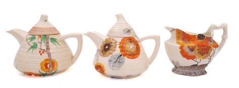 A Clarice Cliff milk jug and two Clarice Cliff Lynton teapots and covers the jug decorated in the