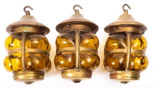 A set of three brass and amber glass ceiling lanterns, in Arts & Crafts taste,