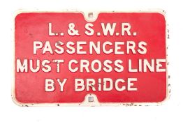 An L&SWR 'Passengers Must Cross Line By Bridge' cast iron sign, white text on a red ground,
