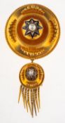 A Victorian Etruscan revival brooch, of ornate circular form with a suspending oval fringe drop,