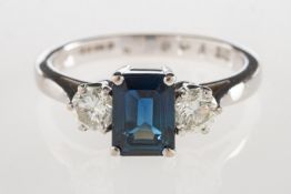 An 18ct gold sapphire and diamond three stone ring, set to the centre with an emerald-cut sapphire,