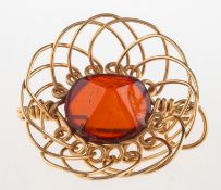 An openwork brooch pendant, set to the centre with a faceted orange paste stone,