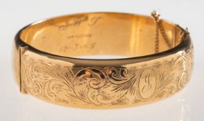 A 9ct gold hinged bangle, with foliate engraving to front panel, safety chain, UK hallmark,