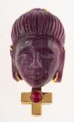 A carved rough ruby pendant brooch, carved in the form of a Buddha's head with a cross below,