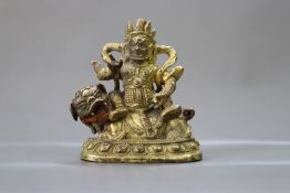 A Sino Tibetan Gilt Bronze figure of Jambhala, seated on his lion, 18/19th century