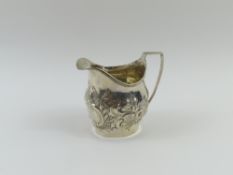 A Georgian silver cream jug, embossed with scrolls