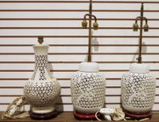 Two white porcelain lamps on wooden base with pierced tree design, a similar cream example with