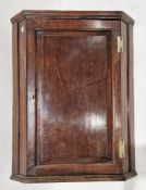 An oak hanging corner cabinet, the single panel door opening to two fixed shelves, 73cm wide by 93cm
