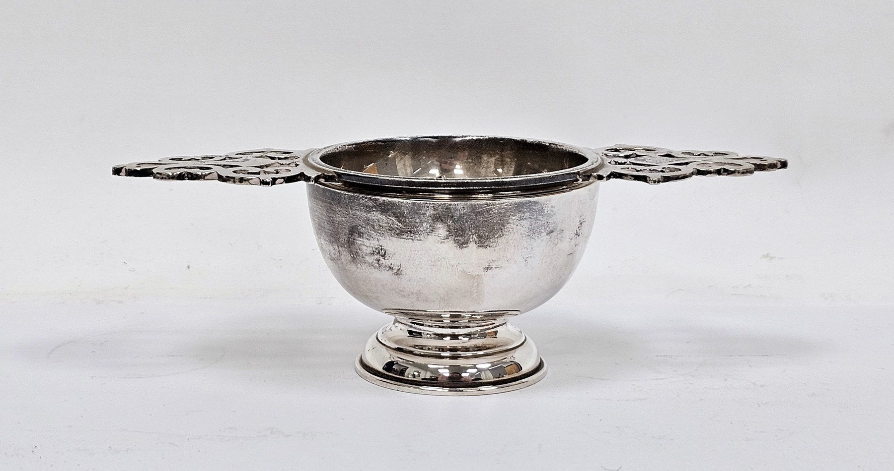 Silver tea strainer, London 1995, Wakely & Wheeler, with ornate pierced twin handles and plain
